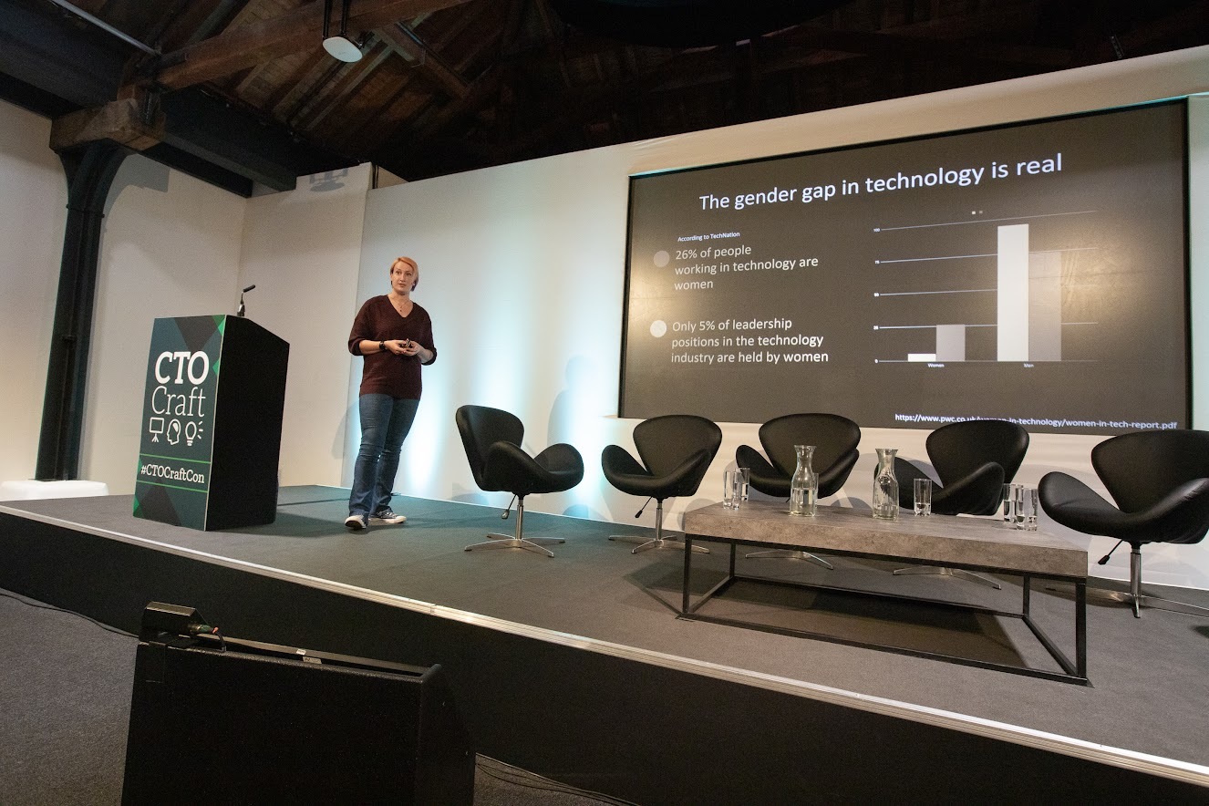 Jen Beattie on stage presenting. Behind her is a large screen where statistics on the gender gap in technology